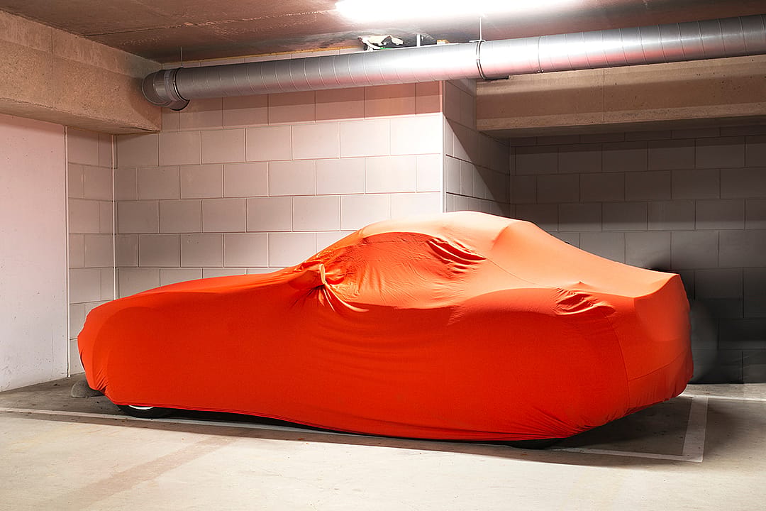 A modern luxury car with an orange-colored protection cover parked in a basement garage.
